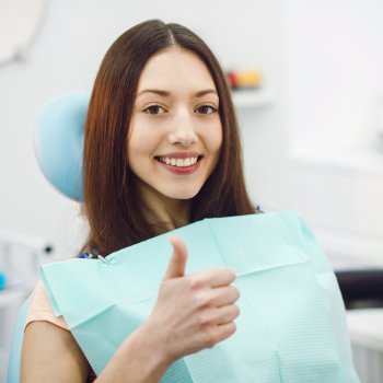 A satisfied young woman sitting in the dentist chair and showing her thumb up