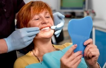 A dentist and a woman after dental implant restoration treatment looking at her teeth in a mirror
